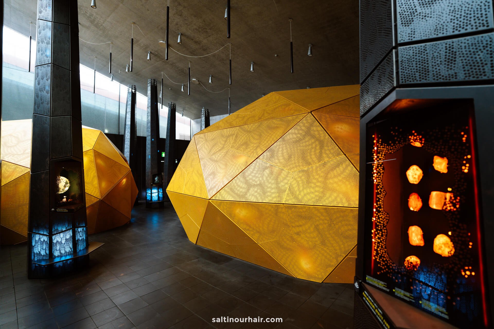 Interior of a modern exhibition space in Tirpitz Museum , perfect for your Denmark itinerary, featuring large yellow geometric structures, illuminated display cases, and tall black columns under a concrete ceiling.