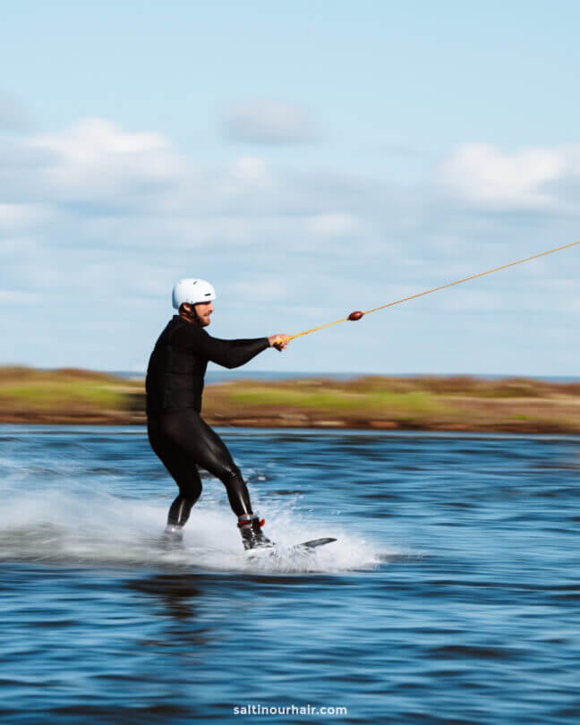 A person wearing a helmet and wetsuit is wakeboarding on a body of water, holding onto a tow rope—an exciting adventure to consider adding to your Denmark itinerary.