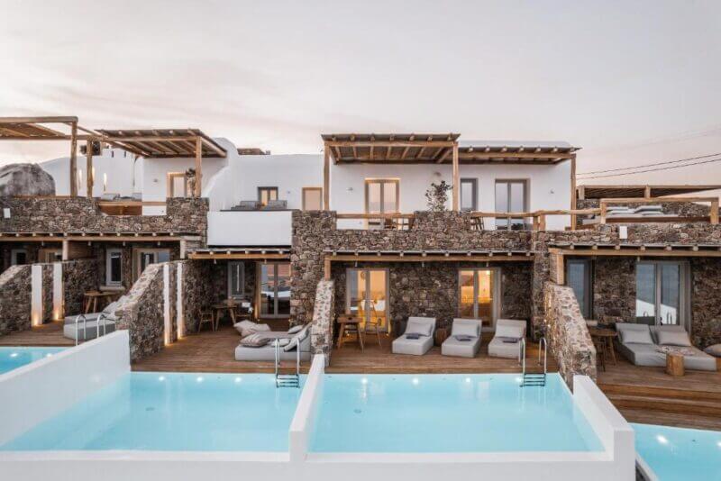 Modern two-story villas with stone and white walls, private decks, lounge chairs, and individual swimming pools at sunset—ideal for those seeking the best hotels in Greece.