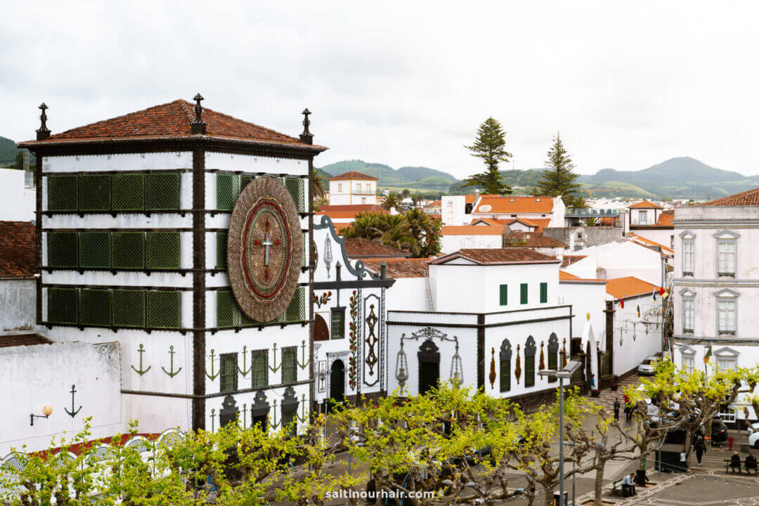 Igreja Matriz de S&atilde;o Sebasti&atilde;o in Ponta Delgada Azores with a large clock tower and green accents, surrounded by white buildings and trees, set against hills