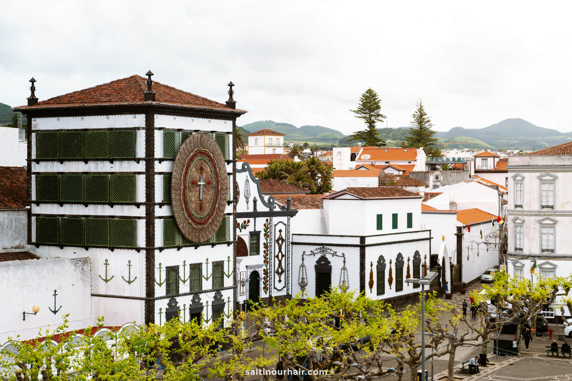 White church with a large clock tower and green accents, surrounded by white buildings and trees in Ponta Delgada - the perfect place to rent a car in azores