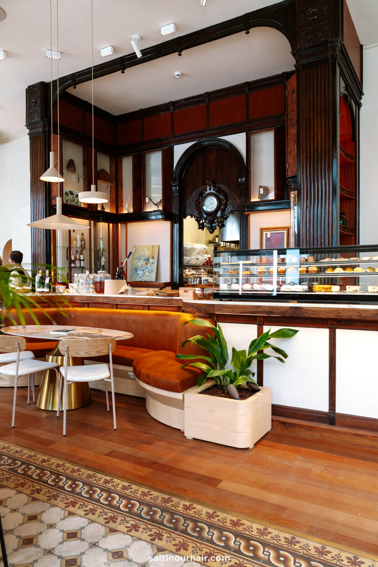 A stylish caf&eacute; interior in Ponta Delgada, featuring a curved orange bench, white tables and chairs, a large decorative clock, pastry display case, and ornate wood paneling