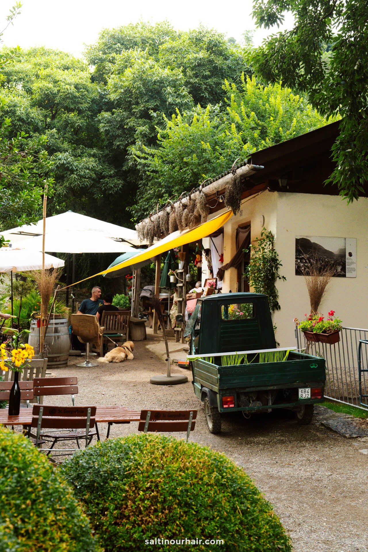 Outdoor café with wooden tables and vintage green Piaggio car under a shaded area in merano italy
