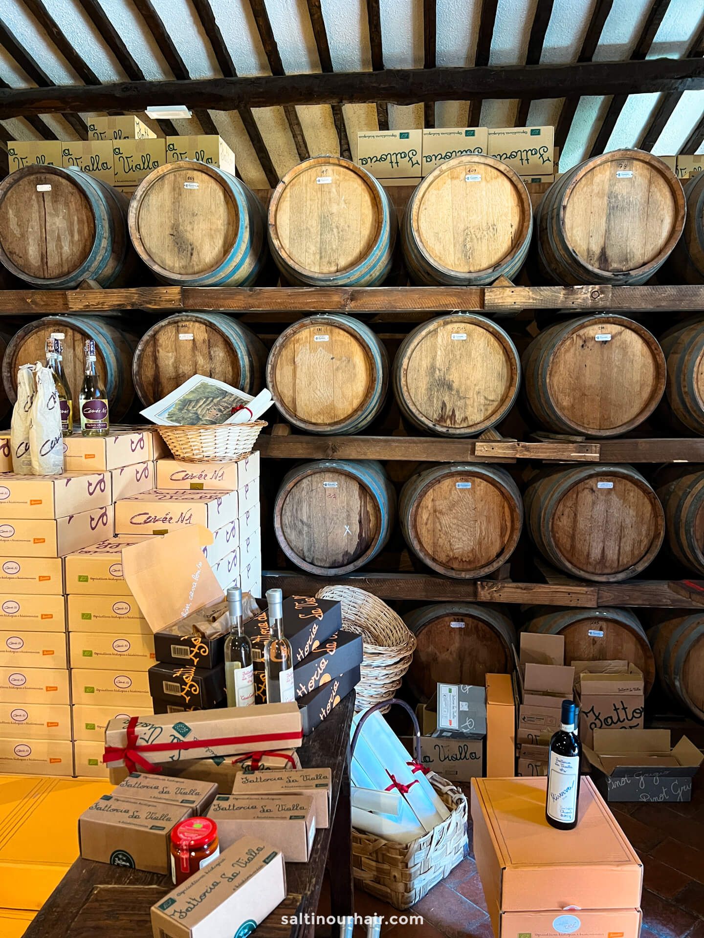 Wooden barrels are stacked on shelves above boxes and bottles, at the cellar of a Tuscany farm in Italy.
