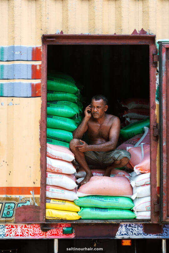A shirtless man sits on stacked bags inside a truck at Pettah market in Colombo, Sri Lanka.