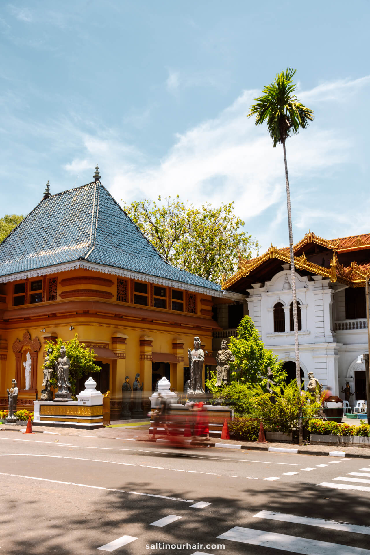 A street view of a yellow building with a blue roof and a white building with ornate trim in Colombo, Sri Lanka