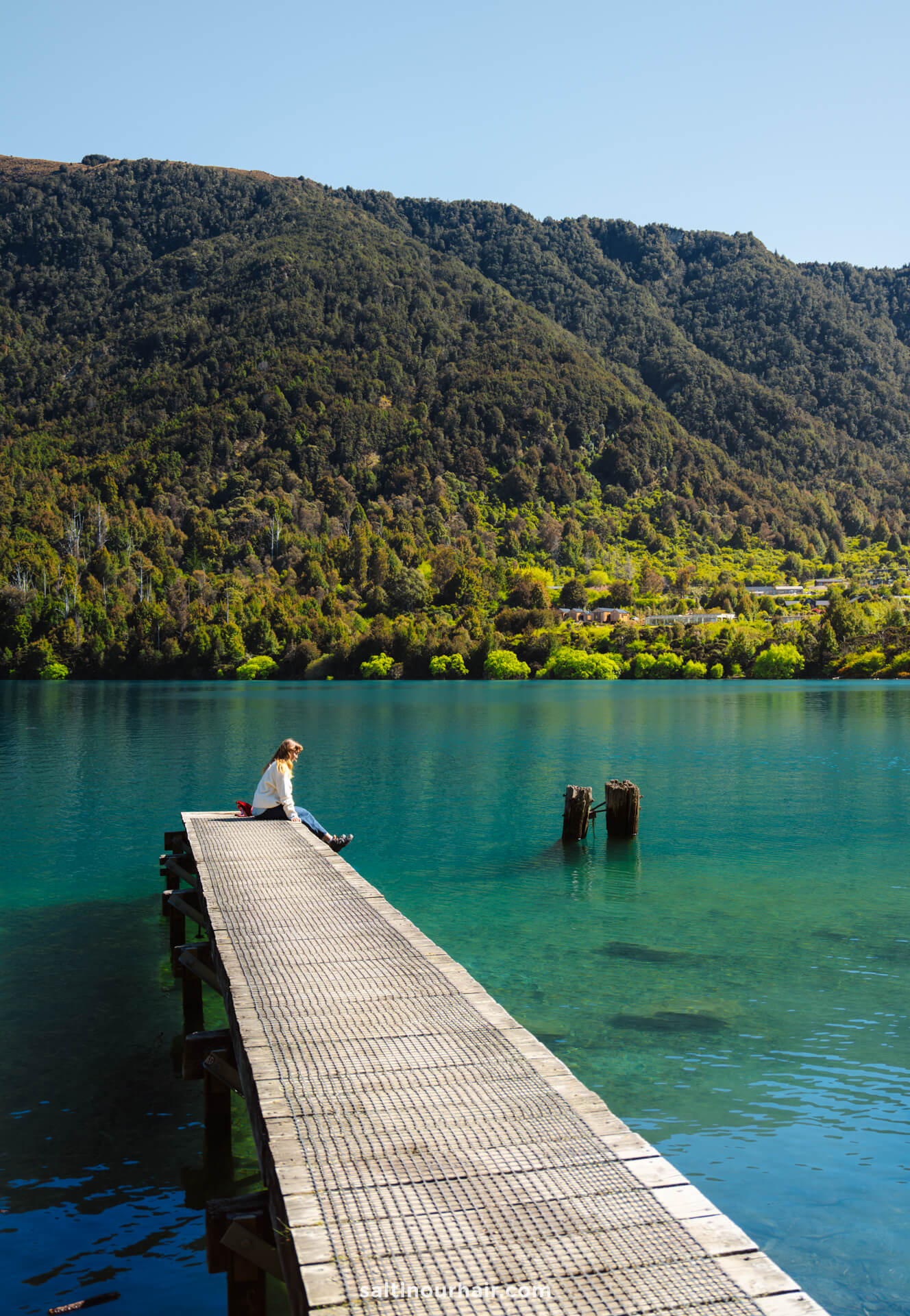 A person sits at the end of a wooden dock over a clear blue lake at Bob
