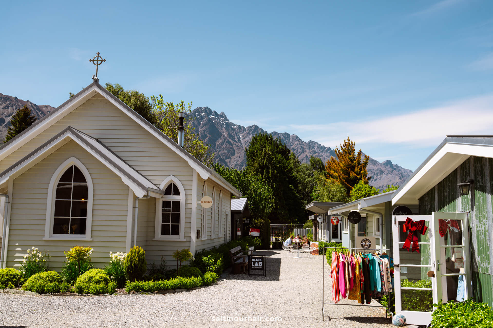 A small, chapel-like building and shops with colorful clothes on racks offer a charming stop among the mountains and clear blue sky&mdash;one of the unique things to do in Queenstown, new zealand.