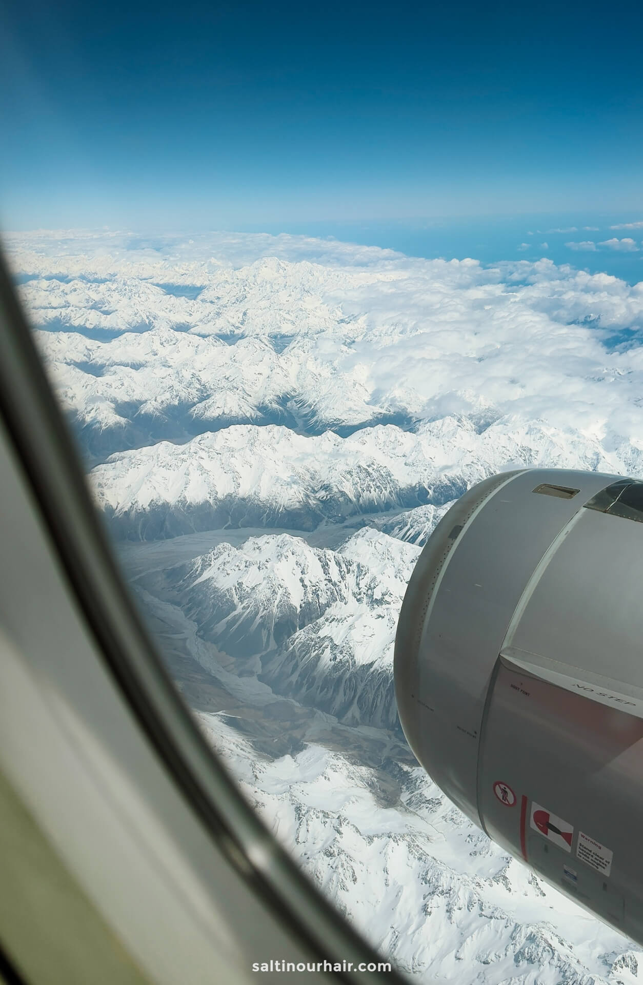 View from an airplane window showing a jet engine and a vast snowy mountain range under a clear blue sky&mdash;perfect inspiration as you plan things to do in Queenstown.