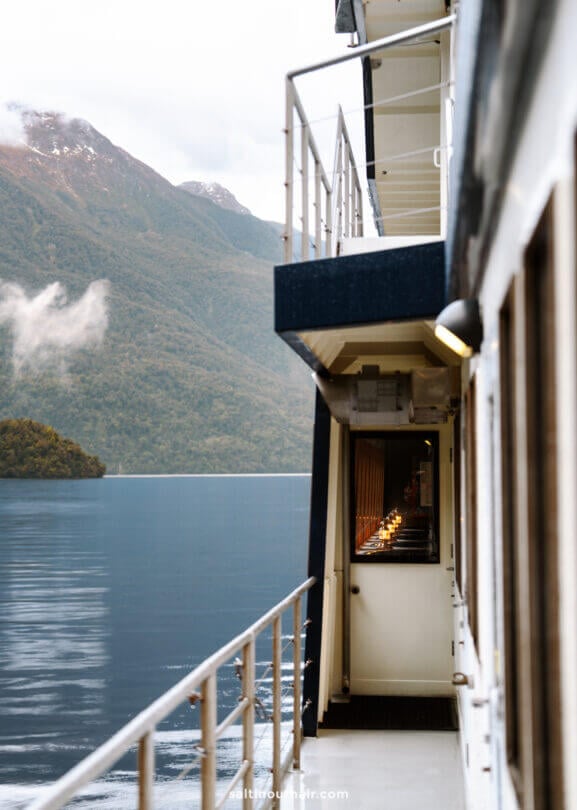 A view from the side deck during an overnight cruise on Doubtful Sound, New Zealand, looking out at calm water and forested mountains in the background.