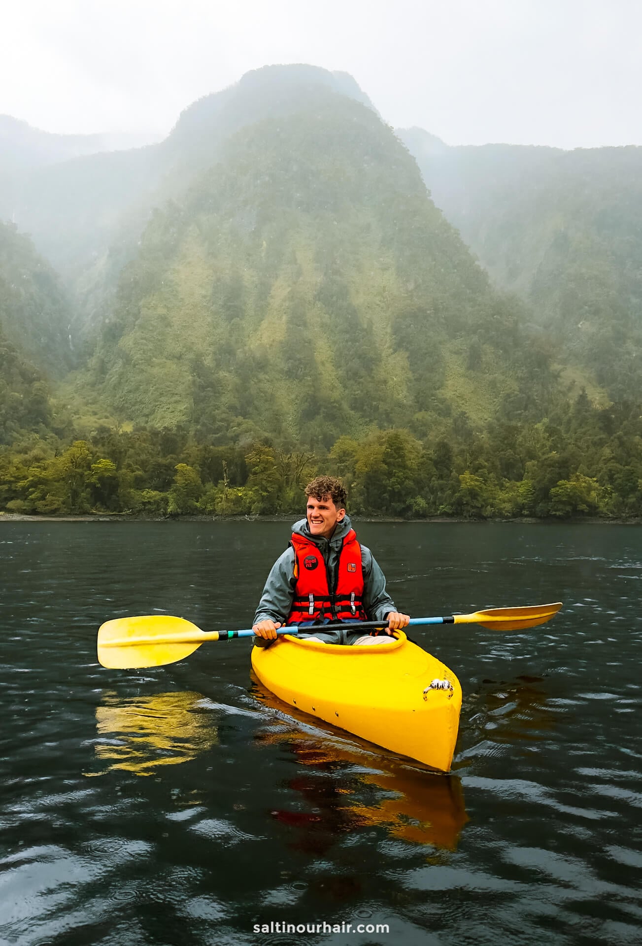 A person in a yellow kayak paddles on a calm lake in doubtful sound, new zealand