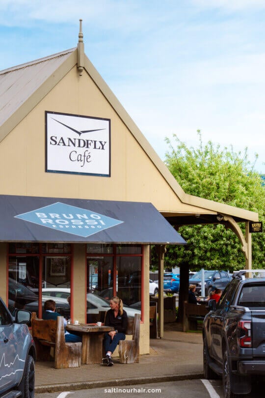 A woman sits at an outdoor table in front of Sandfly Caf&eacute; in Te Anau.