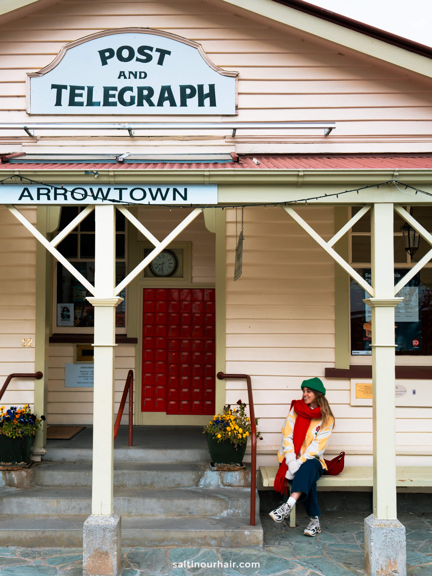 A woman in colorful clothes sits on a bench outside the historic Post and Telegraph building in Arrowtown, New Zealand&mdash;a charming spot to visit among the many things to do Queenstown offers nearby.