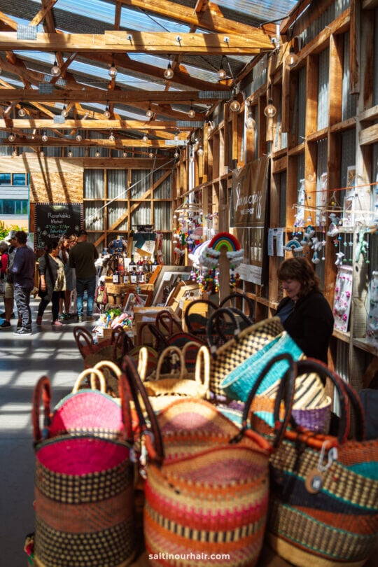Remarkables Market stall inside a wooden building displays woven baskets, crafts, and handmade goods, with people browsing in the background&mdash;one of the unique things to do in Queenstown for those seeking local treasures.