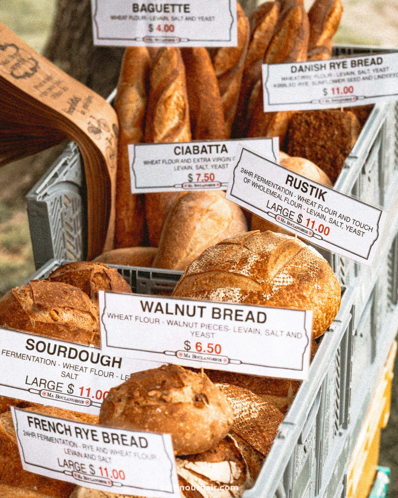 A display of various Arrowtown loaves, each labeled with its name and price, including baguette, ciabatta, walnut bread, rustik, sourdough, Danish rye, and French rye bread.
