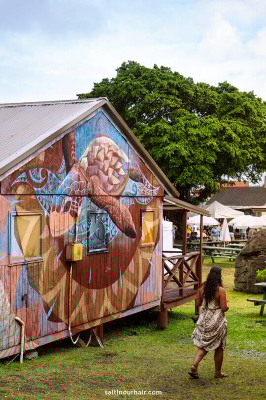 A woman walks toward a wooden building featuring a large sea turtle mural, one of the unique sights among the many things to do in Rarotonga, Cook Islands