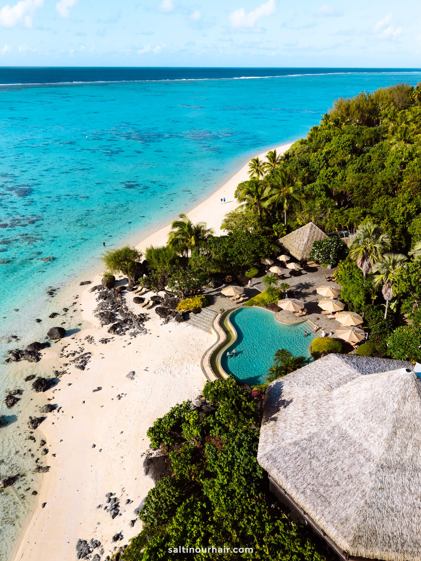 Aerial view of a tropical resort with a pool, palm trees, sandy beach, and clear turquoise ocean water&mdash;perfect for discovering the top things to do Rarotonga has to offer.