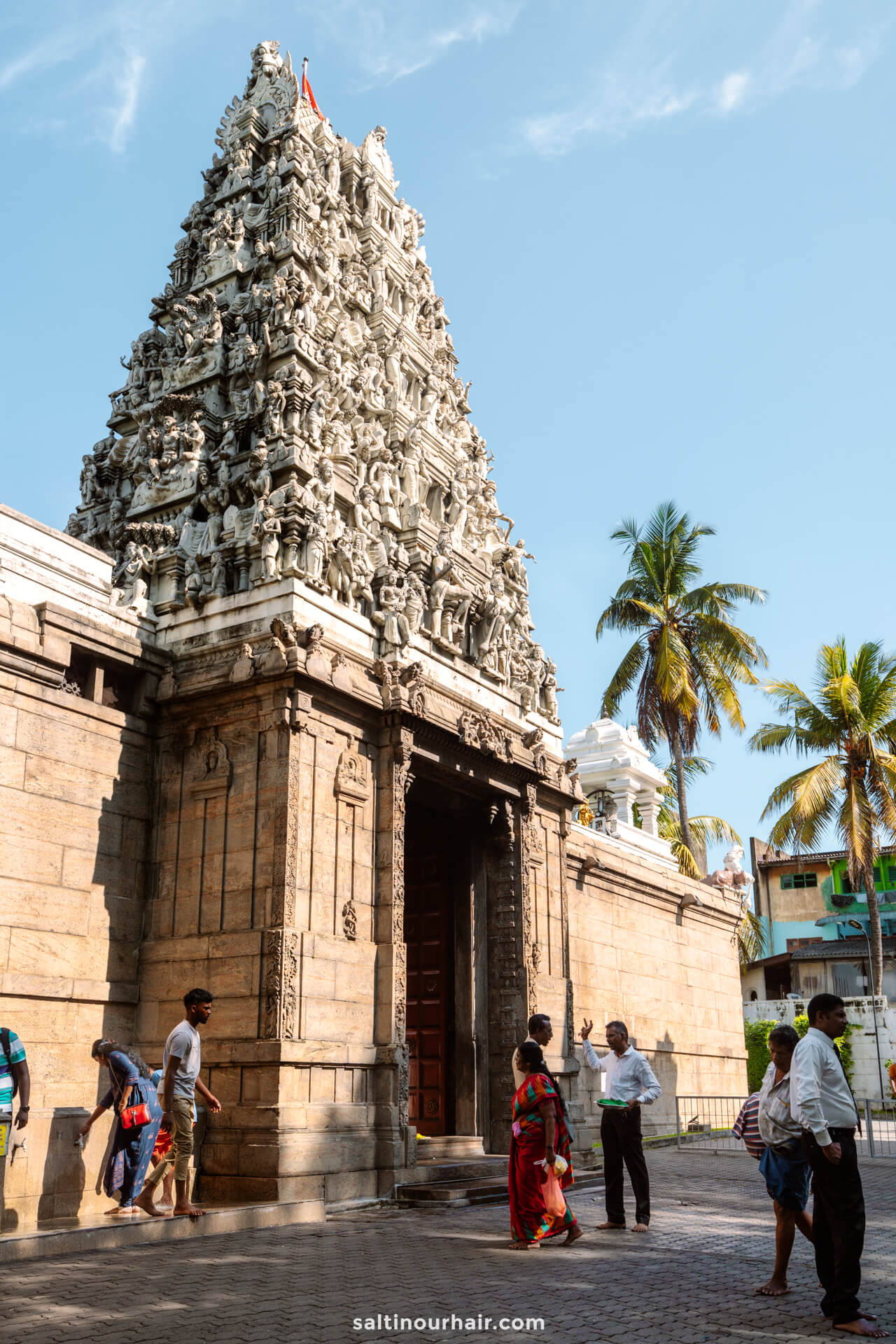 Tall stone temple entrance with intricate carvings, people standing and walking nearby-classic scene in Colombo, Sri Lanka.