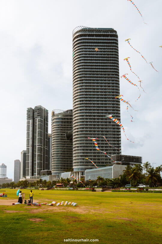 Tall modern skyscrapers rise behind a grassy open area where people are flying colorful kites&mdash;one of the popular things to do in Colombo.