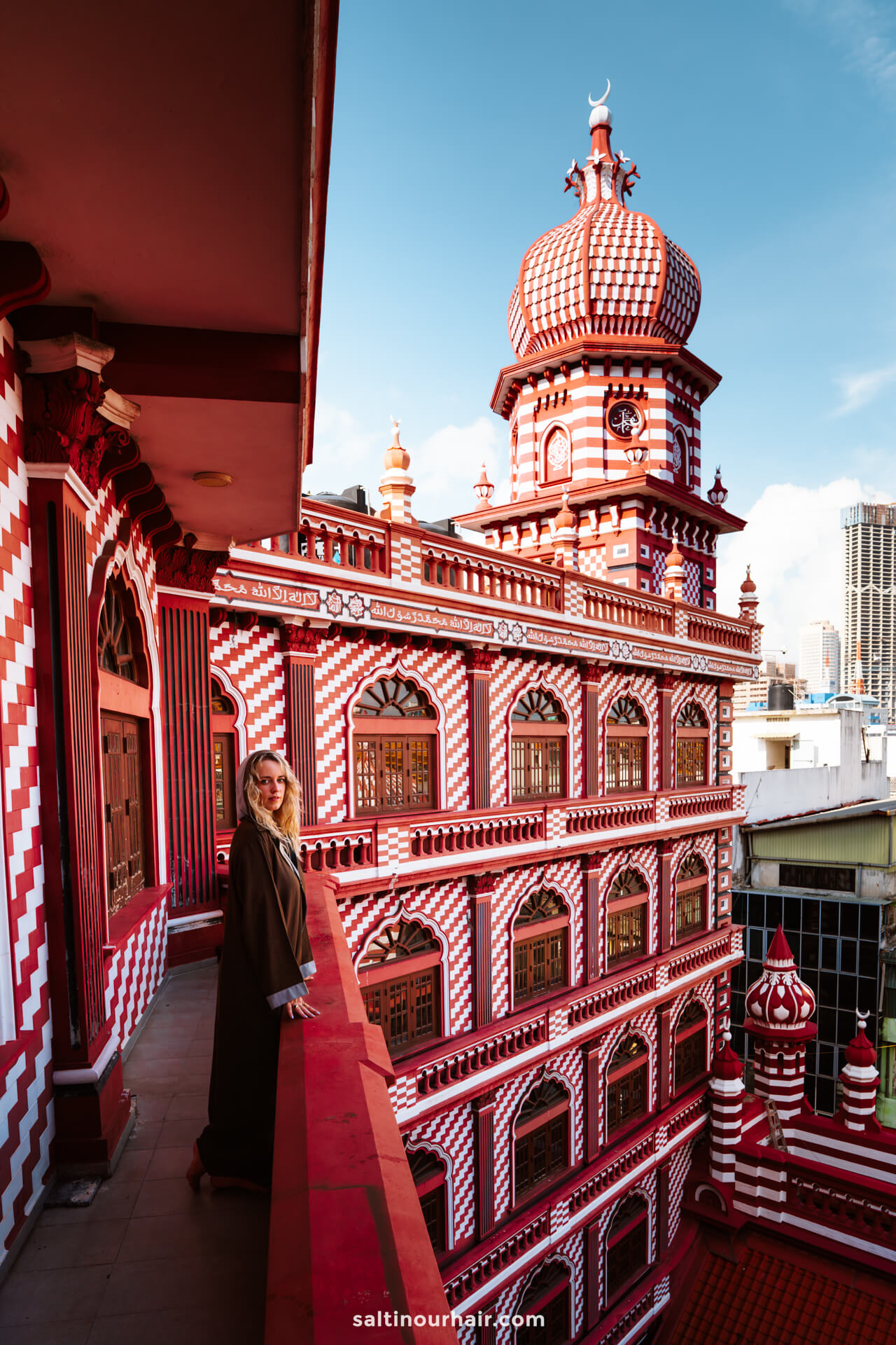 A person stands on a balcony overlooking the red-and-white patterned Jami Ul-Alfar Mosque in Colombo, Sri Lanka&mdash;a must-see for anyone exploring the top things to do Colombo.