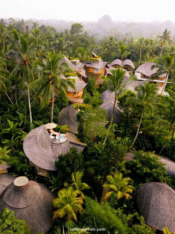 Aerial view of eco-friendly, dome-shaped bambootel villas nestled among dense tropical trees, with two people standing on a rooftop terrace.