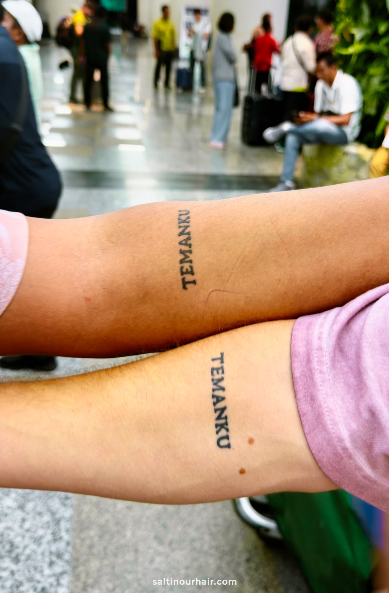 Two forearms with matching black tattoos reading TEMANKU in Indonesian language