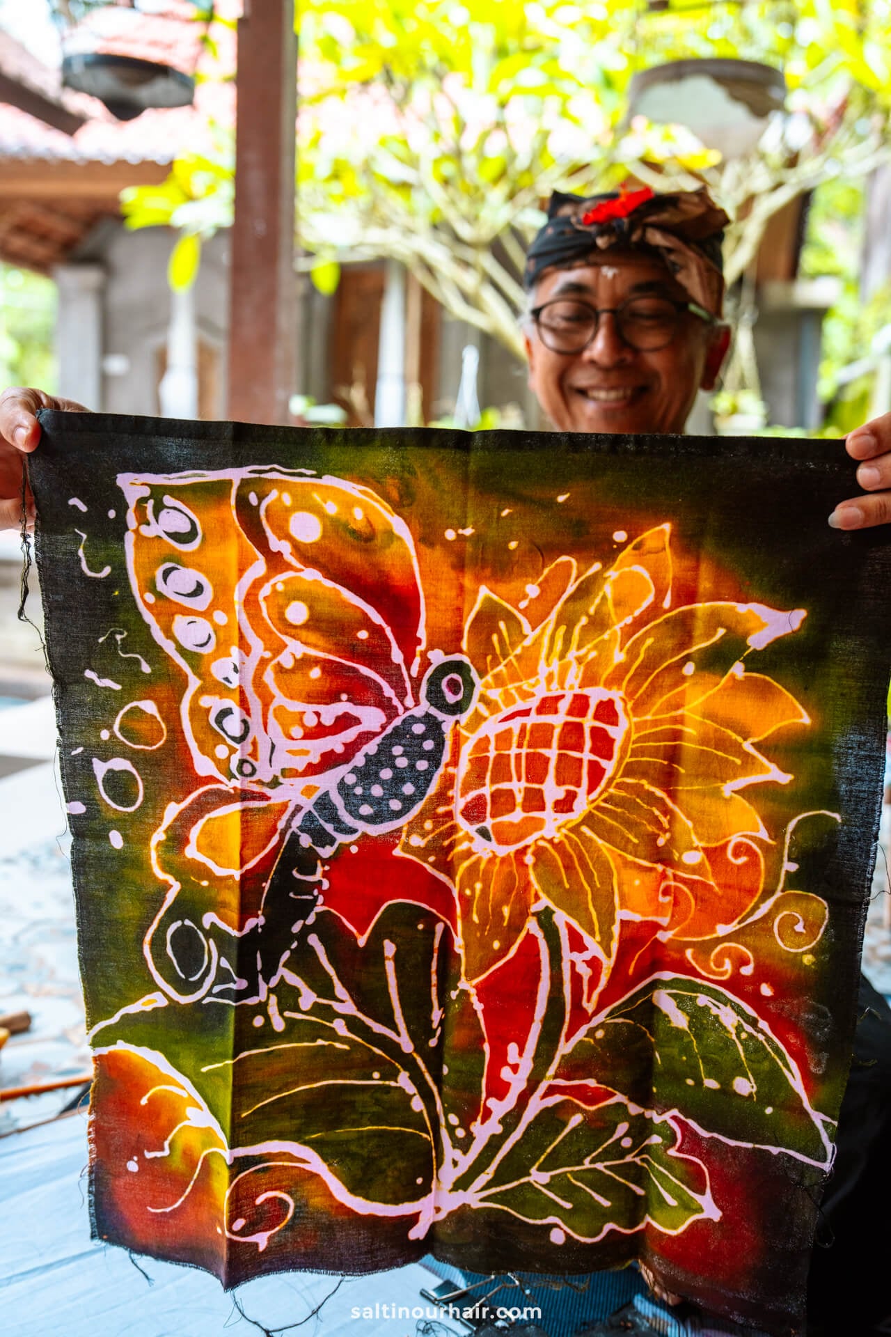 A balinese man proudly displays their creation from a batik painting workshop in bali