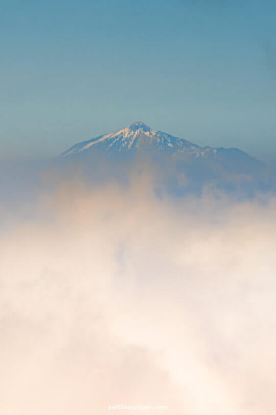 Snow-capped mountain peak rising above a layer of clouds under a clear blue sky—discover this breathtaking view on La Palma, the hidden gem of the Canary Islands.