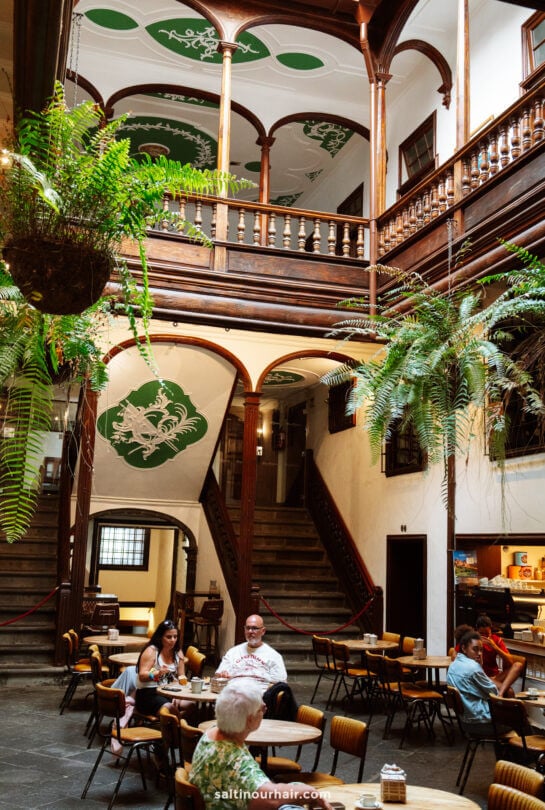 Spacious indoor courtyard with wooden balconies, green ceiling art, hanging ferns, and people seated at tables in a café setting—ideal for a La Palma travel guide to the hidden gems of the Canary Islands.