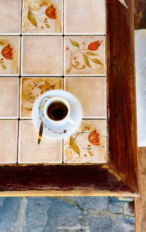 A cup of coffee on a saucer sits atop a tiled table with floral patterns and a wooden border, evoking the charming cafes found in La Palma, Canary Islands.